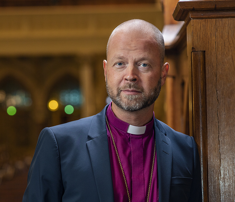 Papin pukuun pukeutunut mies katsoo kameraan.