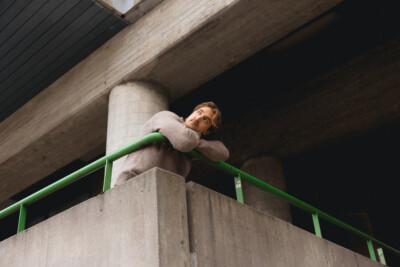 Nuori henkilö nojaa betonikaiteeseen teollisessa ympäristössä ja katsoo mietiskelevästi yläviistoon.