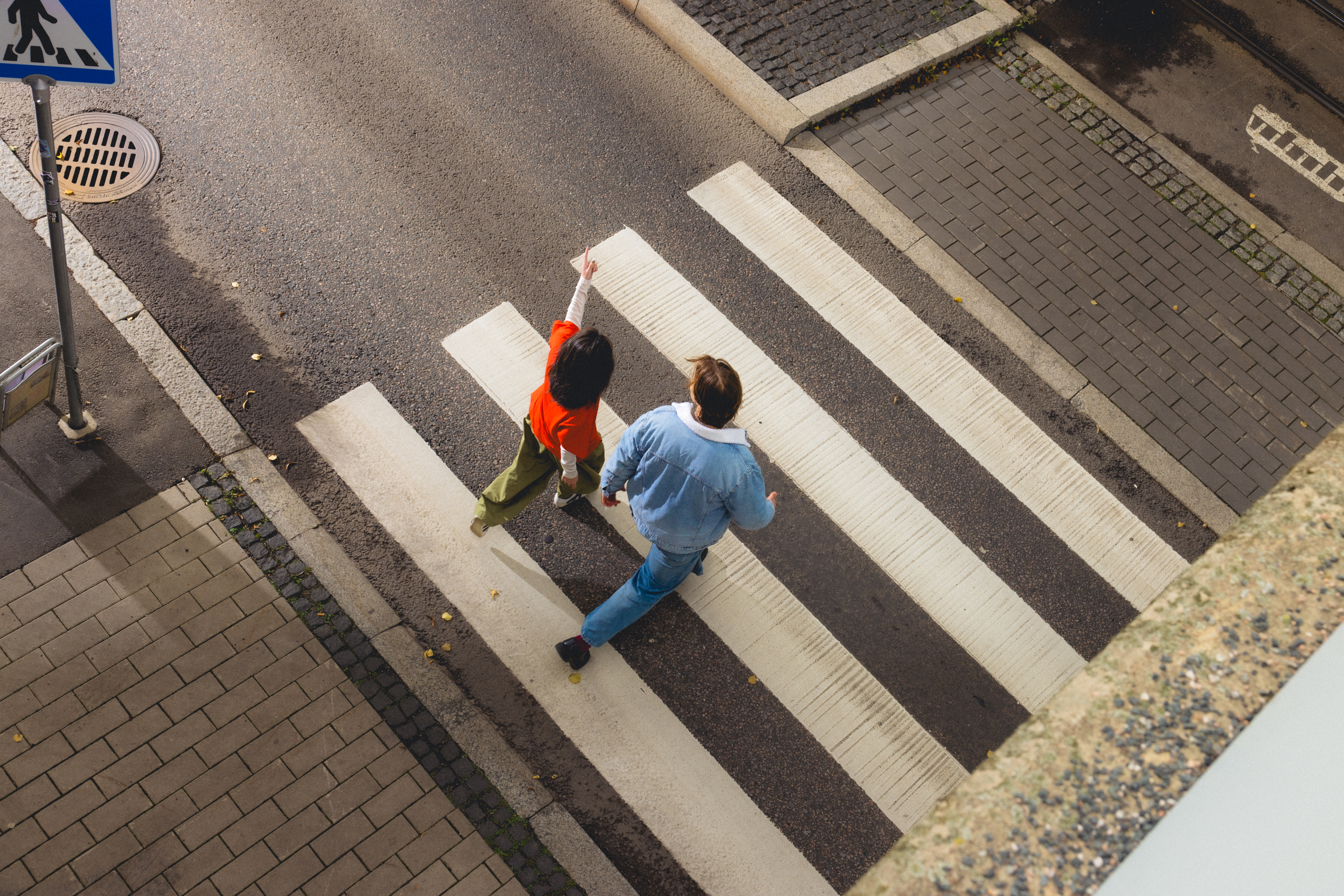 Kuva ylhäältä päin kahdesta ihmisestä, jotka kävelevät suojatiellä kaupungin kadulla.
