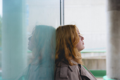 Nuori nainen nojaa selällään ikkunaa vasten ja katsoo sivulle mietteliäänä.