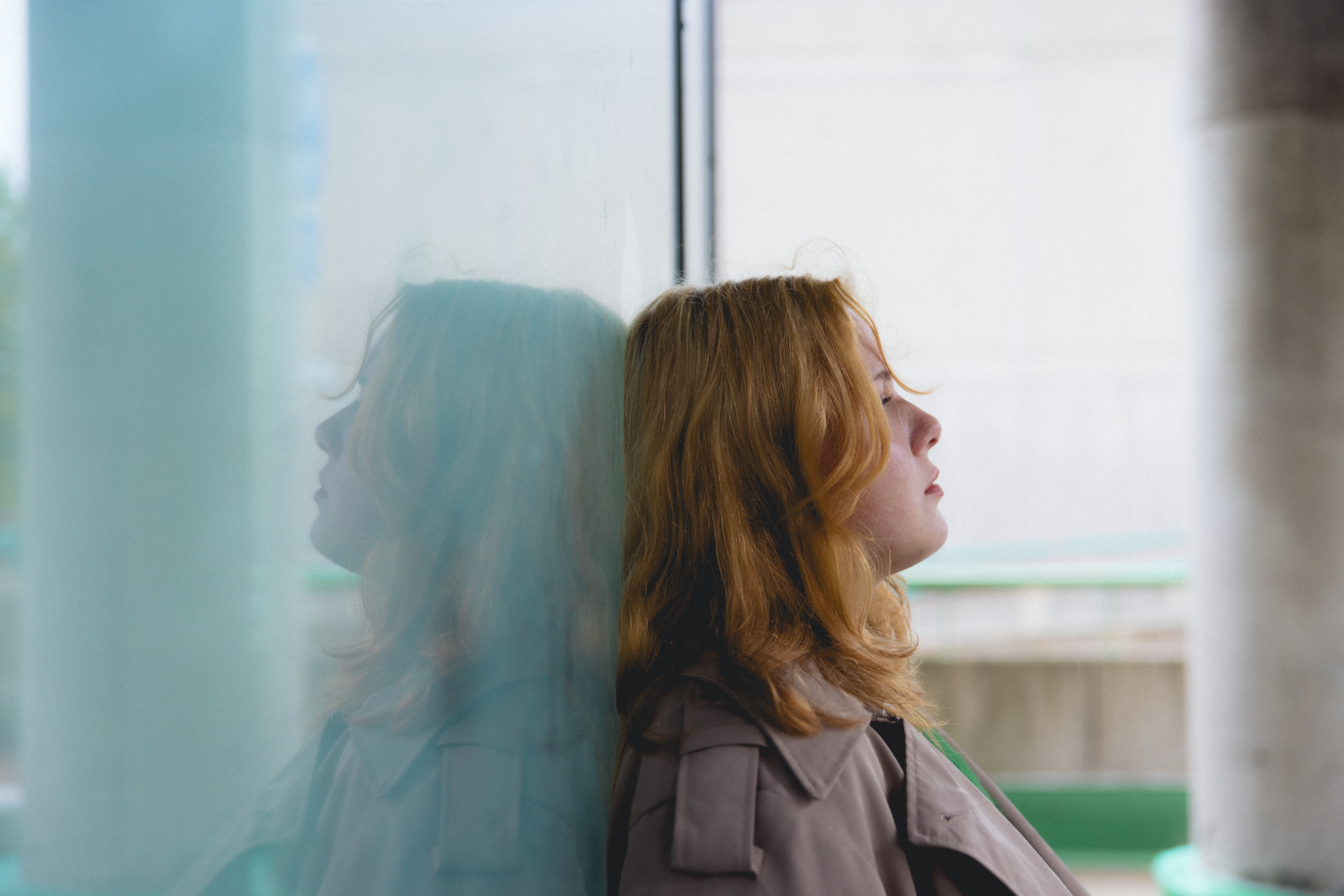 Nuori nainen nojaa selällään ikkunaa vasten ja katsoo sivulle mietteliäänä.