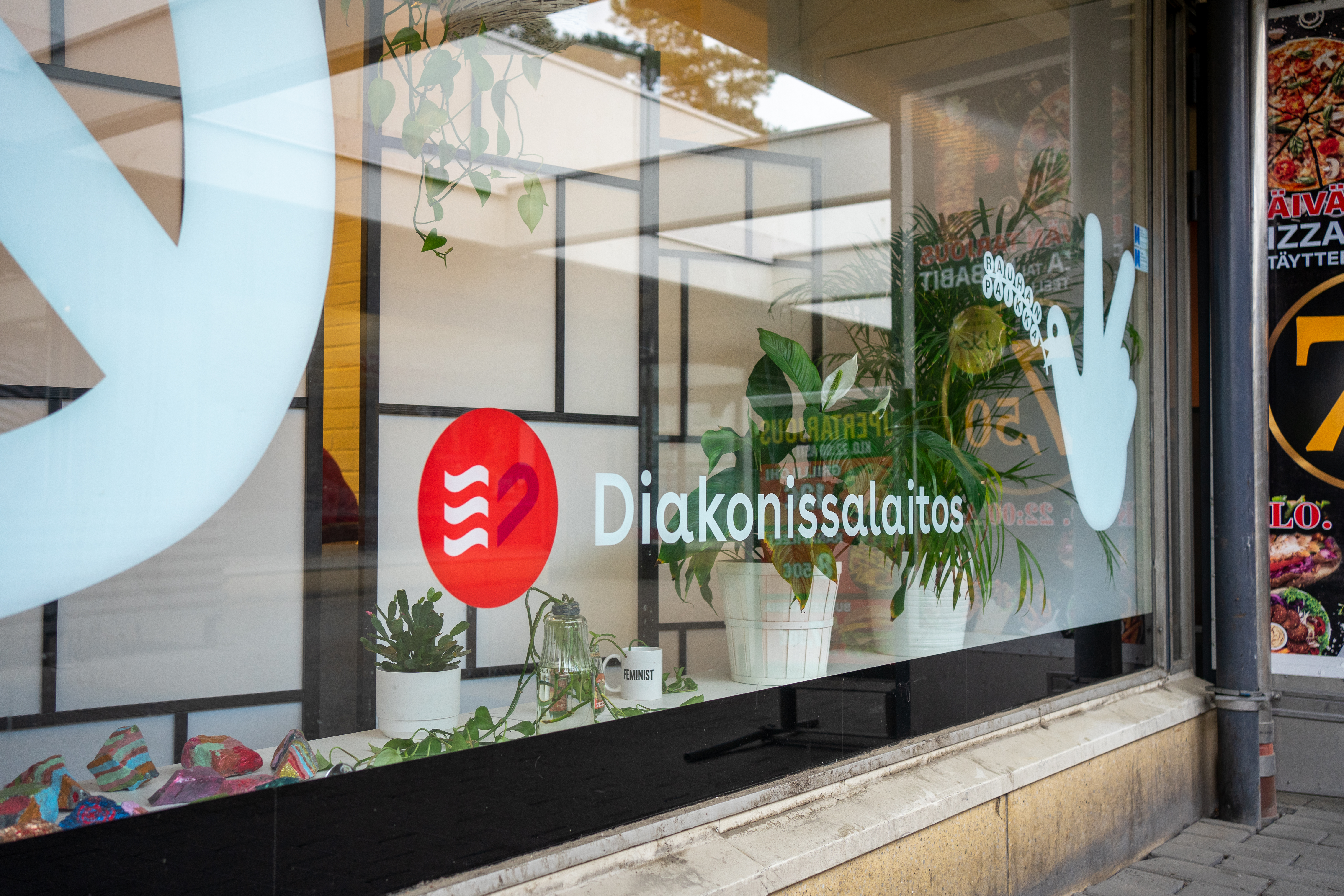 Diakonissalaitoksen logo ja nimi näkyvät Kontulan D-aseman ikkunassa, taustalla näkyy kasveja.