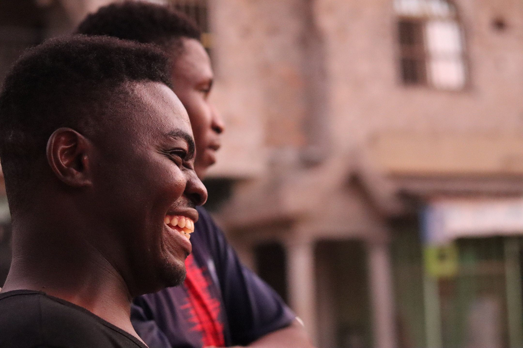 Kaksi henkilöä hymyilemässä ja katsomassa eteenpäin, taustalla epätarkka rakennus.