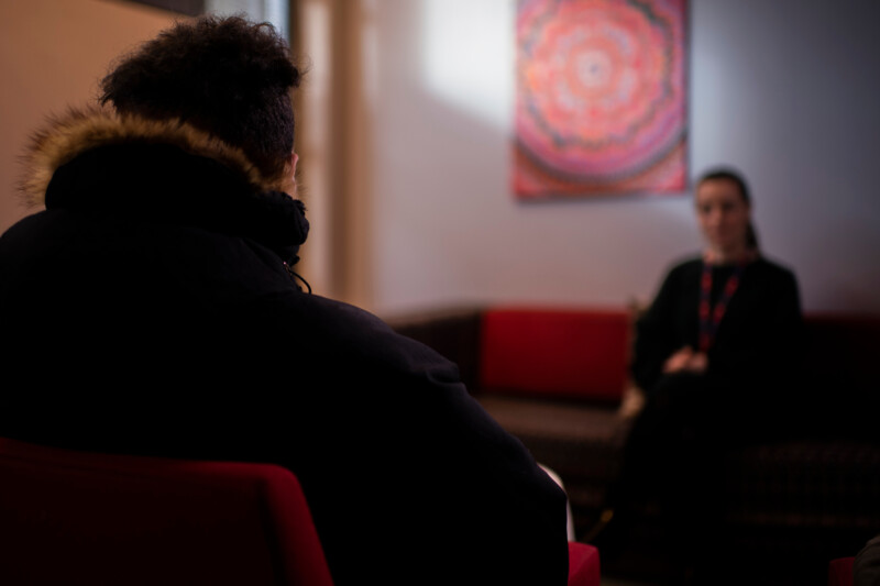 Two people seated and engaged in conversation in a softly lit room with a colorful abstract painting on the wall.