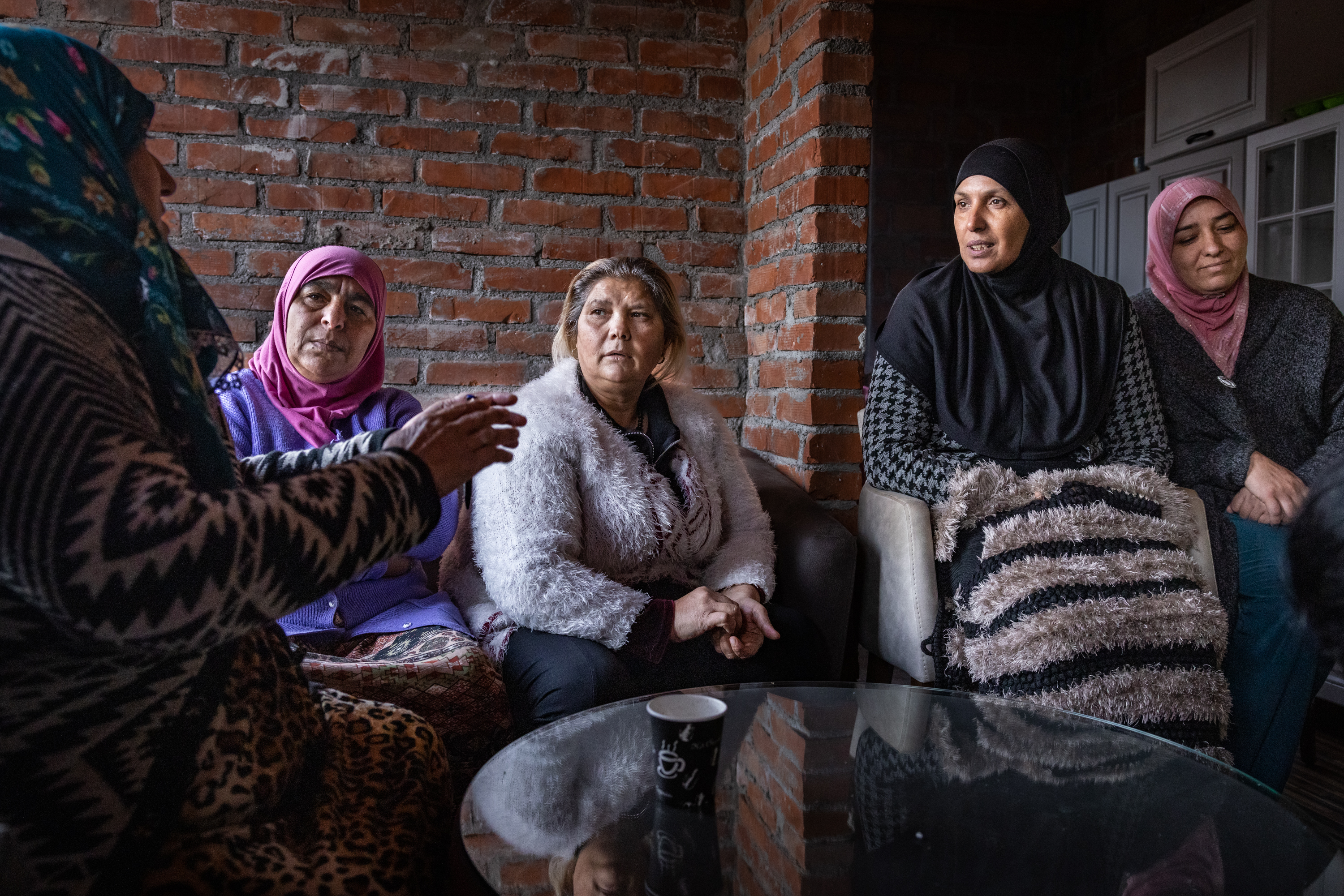 Viisi naista istuu yhdessä pöydän ympärillä keskustellen tiiliseinän edessä.