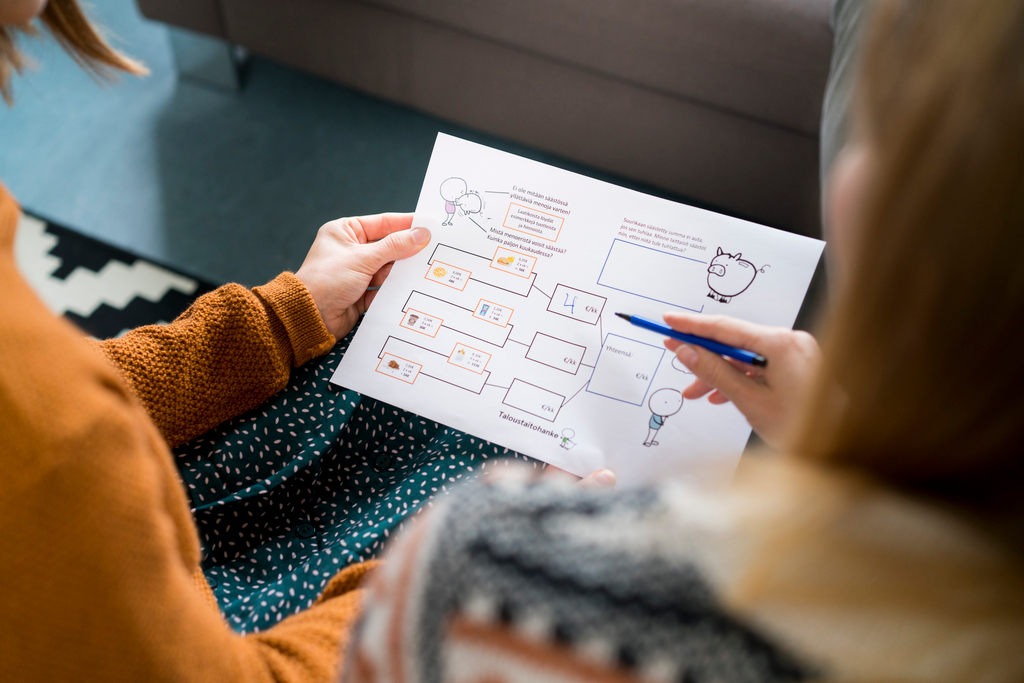 Kaksi henkilöä istuu sohvalla ja tarkastelee yhdessä talousaiheista kaaviota, jossa on piirroksia kuten säästöpossu ja lamppu.