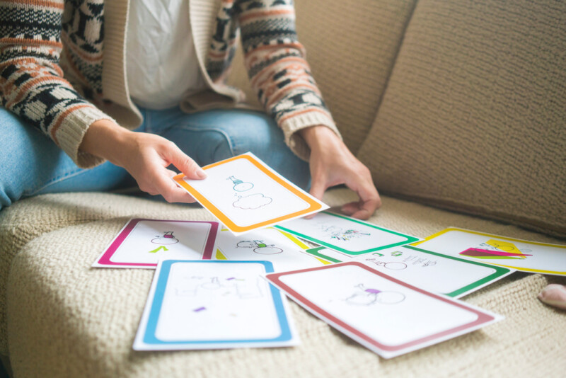 Henkilö istuu sohvalla ja järjestelee värillisiä kortteja, joihin on piirretty erilaisia kuvia.