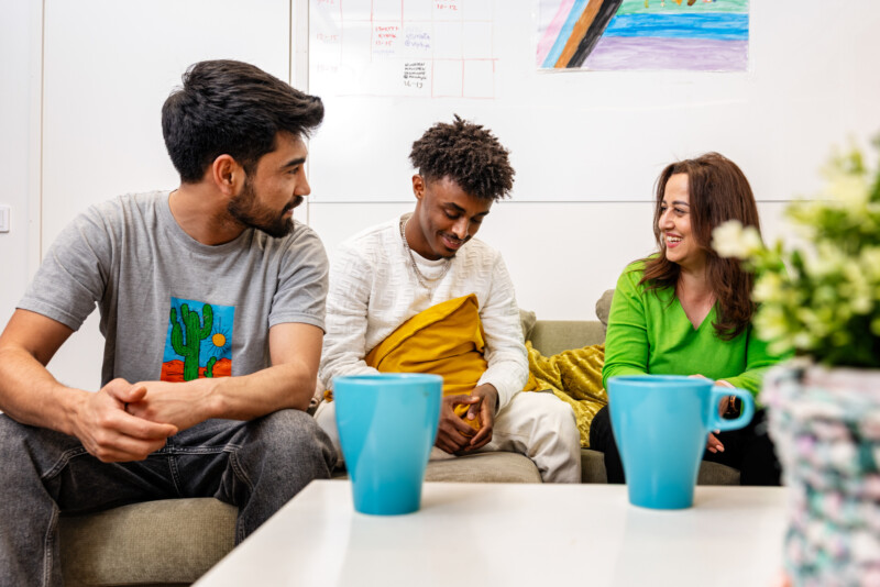 Nuori mies maalaamassa värikästä esinettä pöydän ääressä, taustalla toinen nuori nainen maalaamassa.