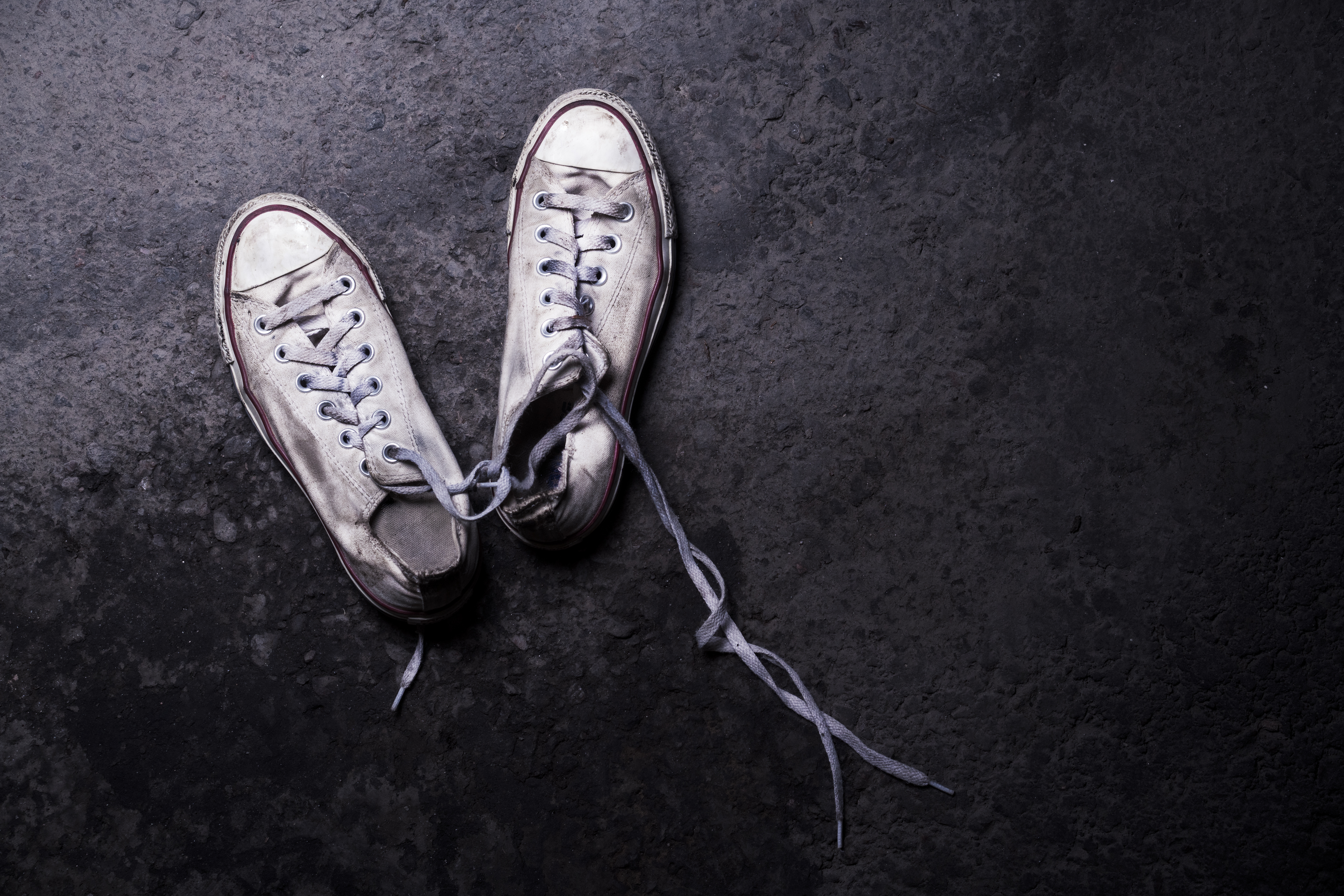 Kuluneet valkoiset tennarit, joiden nauhat ovat osittain irti, mustalla taustalla.