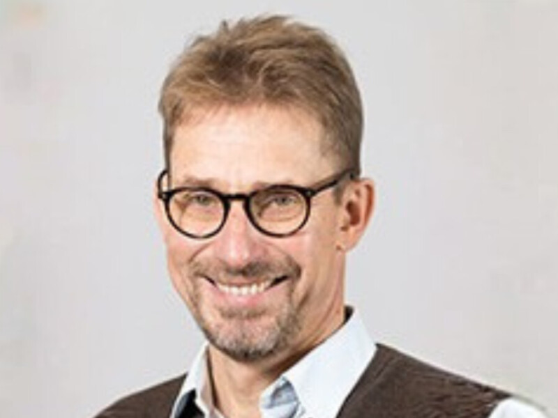 Silmälasipäinen mies katsoo hymyillen kameraan.