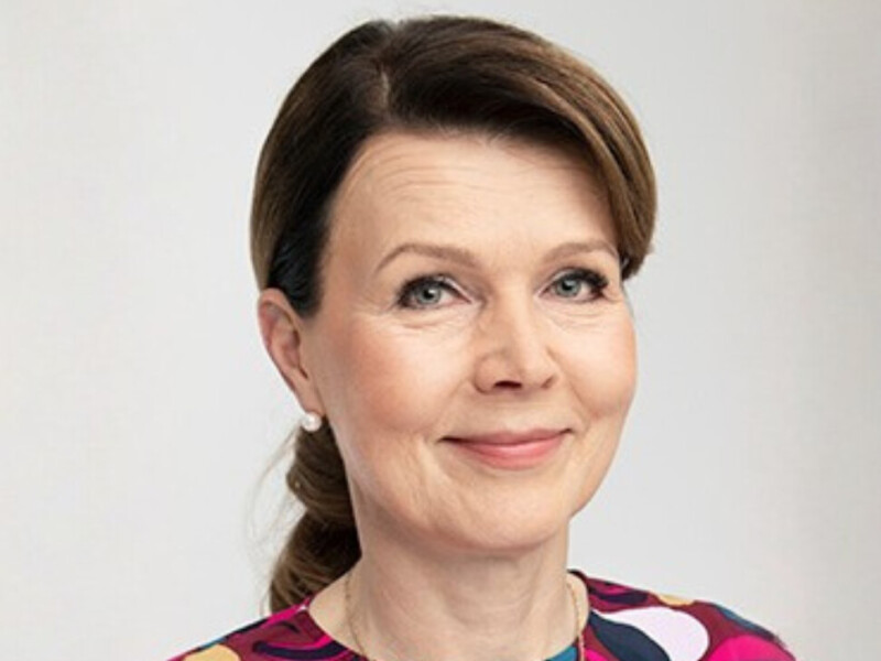 Tummahiuksinen nainen katsoo hymyillen kameraan.