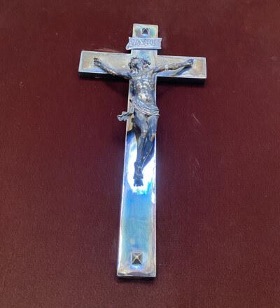 Hopeinen krusifiksi kiinnitettynä punaiseen taustakankaaseen.