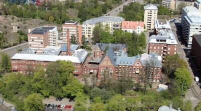 Ilmakuva Diakonissalaitoksen Alppikadun korttelista, jossa näkyy punatiilisiä rakennuksia ja vehreää ympäröivää kaupunkialuetta.