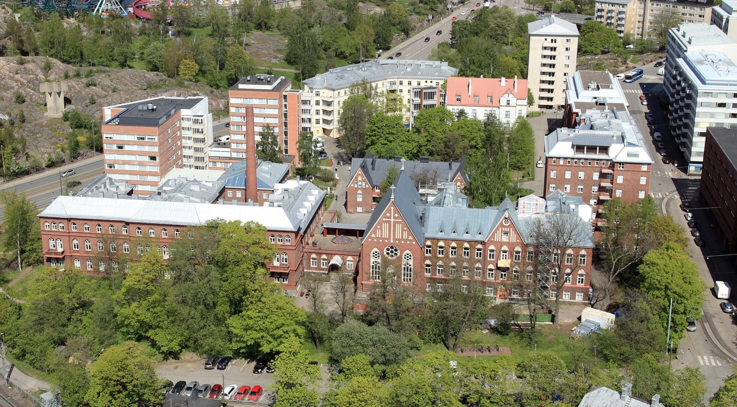 Ilmakuva Diakonissalaitoksen Alppikadun korttelista, jossa näkyy punatiilisiä rakennuksia ja vehreää ympäröivää kaupunkialuetta.