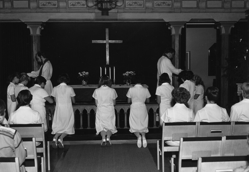 Mustavalkoinen kuva Diakonissalaitoksen kirkon alttarilta 1990-luvulta, jossa useita henkilöitä polvistuneina rukoilemassa alttarin edessä.