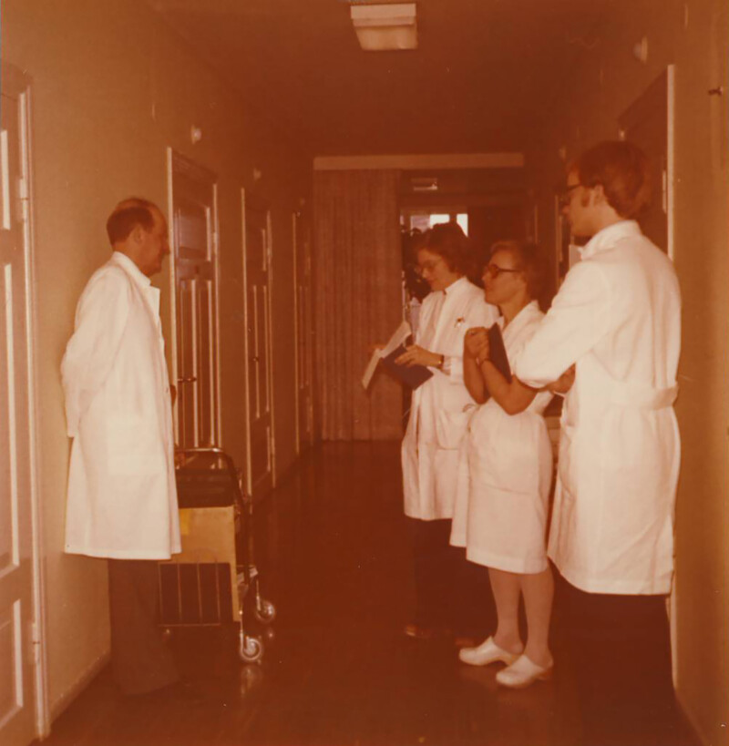 Diakonissalaitoksen sairaalan käytävällä neljä valkokaapuihin pukeutunutta hoitohenkilökuntaan kuuluvaa henkilöä keskustelee.