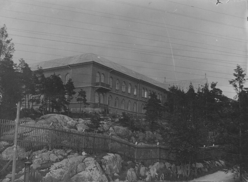Mustavalkoinen valokuva Diakonissalaitoksen sairaalarakennuksesta vuodelta 1898, joka sijaitsee kallioisen ja puuston peittämän mäen päällä.