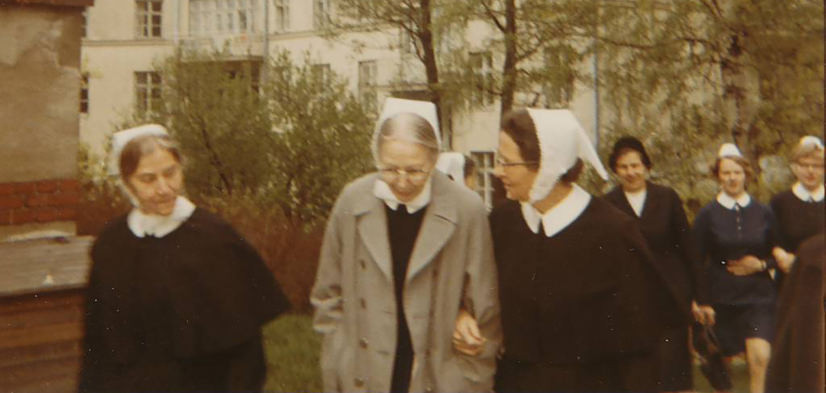 Ryhmänaisia ulkona, suurin osa pukeutuneina diakonissalaitoksen asuihin ja päähineisiin, kävelemässä ja keskustelemassa.