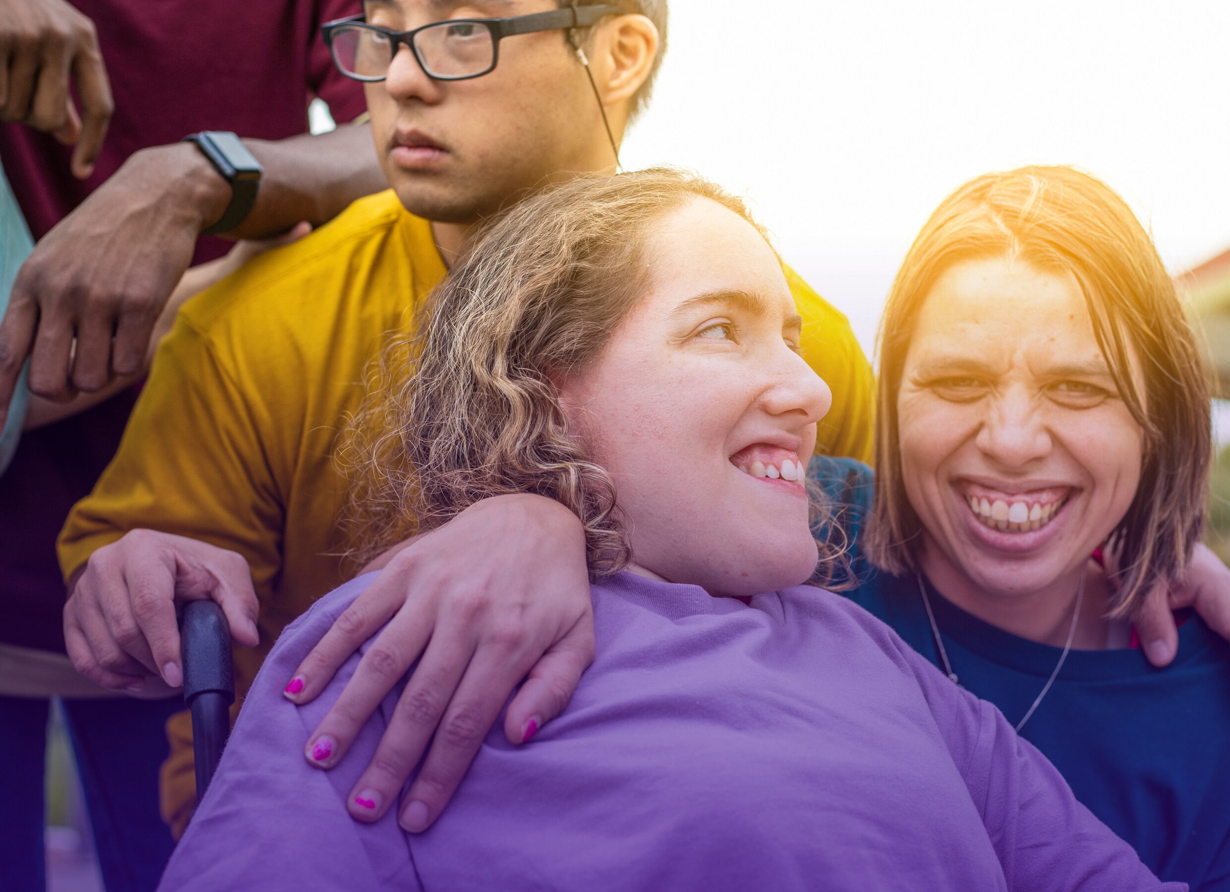 Hymyileviä ihmisiä läheisessä kohtaamisessa, yksi henkilö nojaa toisen olkapäälle, taustalla näkyy lisää ihmisiä.