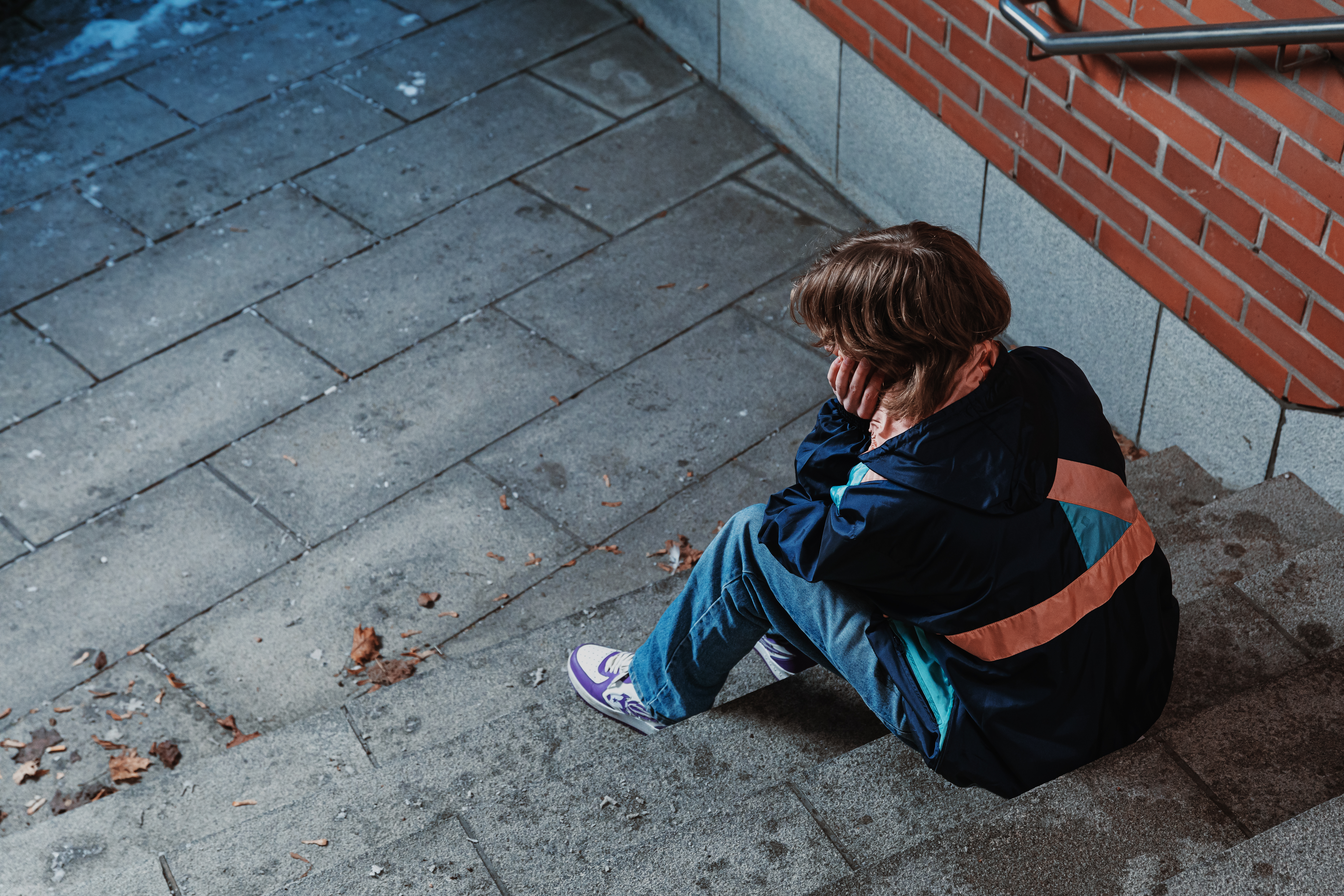 Nuori istuu yksin ulkona betonilattialla kädet poskilla, taustalla tiiliseinä.