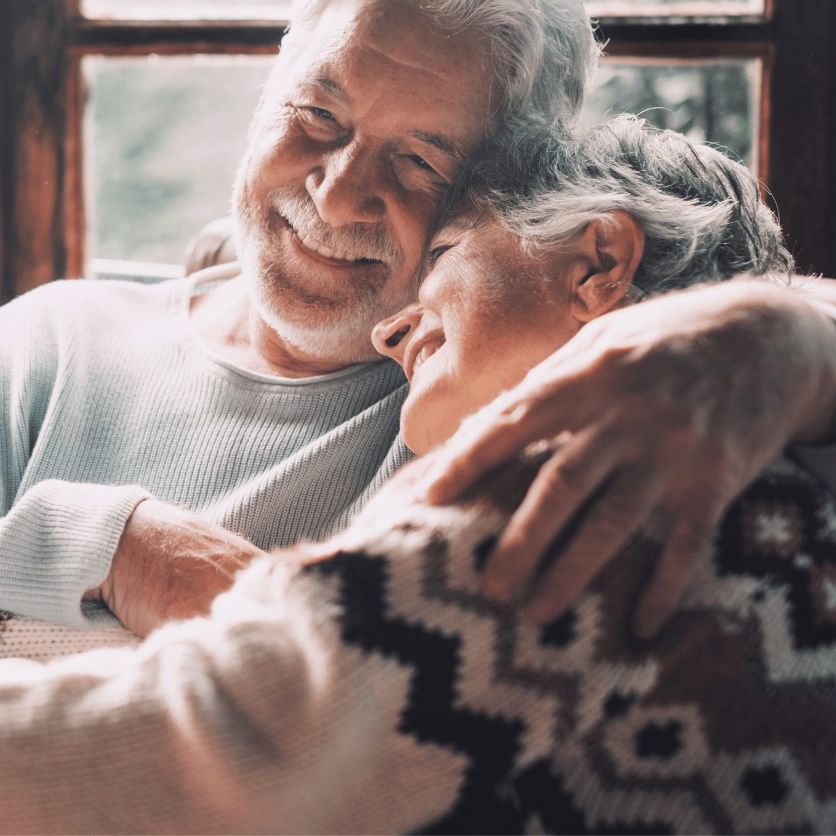 Vanhempi pariskunta hymyilee ja halaa toisiaan lämpimästi kodikkaassa ympäristössä.