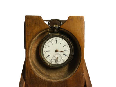 Vanha taskukello puisessa telineessä, jossa kellonajan osoittaa noin kello 15.30.