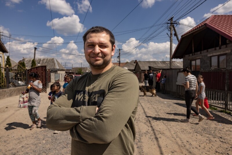 Tummahiuksinen mies katsoo hymyillen kameraan kädet ristissä rinnalla.