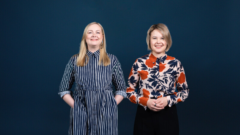 Kaksi naista seisoo rinnakkain ja katsoo hymyillen kameraan.