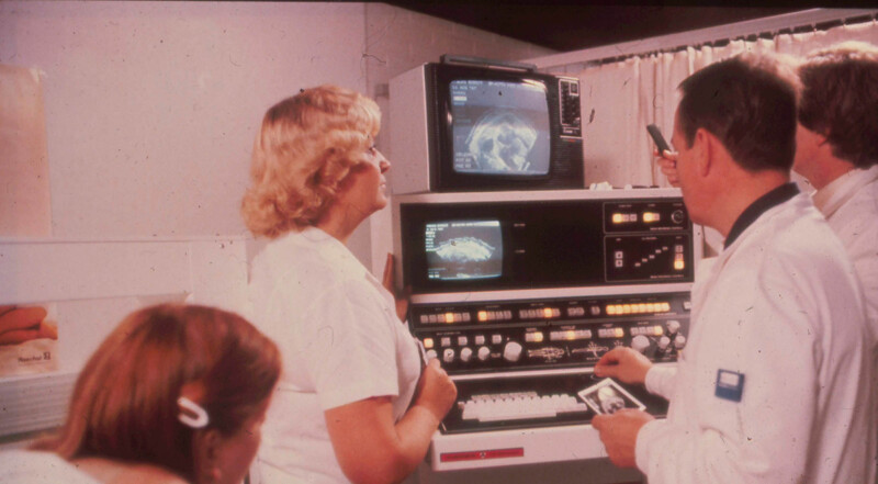 Vuonna 1980 otettu kuva Diakonissalaitoksen sairaalan lääkäreistä ja hoitajista käyttämässä Octoson-laitteistoa potilastietojen ja kuvantamisen hallintaan.