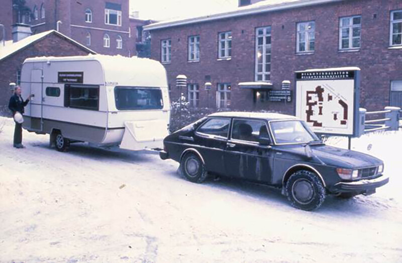 Talvinen kuva, jossa musta auto vetää valkoista asuntovaunua Diakonissalaitoksen sairaalan pihalla vuonna 1979.