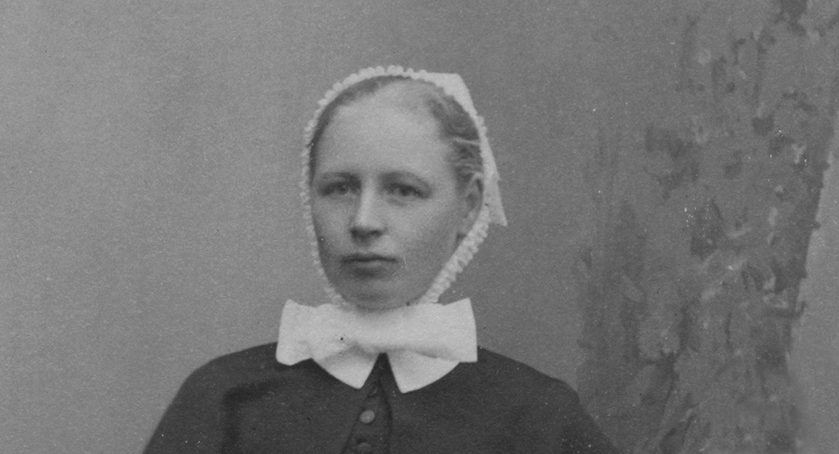 Mustavalkoinen valokuva naisesta, joka pukeutunut vanhanaikaiseen diakonissan asuun, päässään valkoinen päähine ja kaulus, vuodelta 1906.