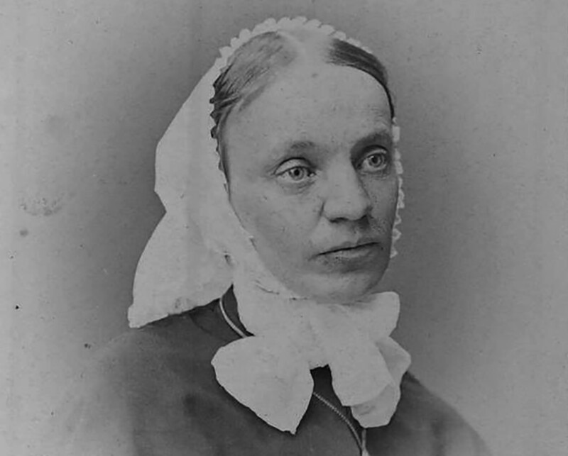 Mustavalkoinen valokuva naisesta, jolla on valkoinen diakonissan päähine ja rusetti leuan alla, katsoo sivulle.