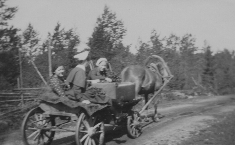 Mustavalkoinen valokuva 1930-luvulta, jossa kolme henkilöä istuu hevosvetoisessa vaunussa metsäisen tien varrella.