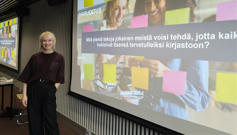 Vaaleahiuksinen nainen katsoo hymyillen kameraan.