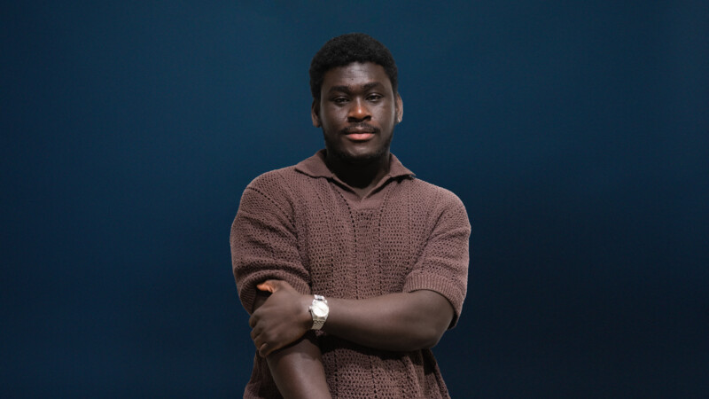 Ruskeaan villapaitaan pukeutunut nuori mies katsoo vakavana kameraan.