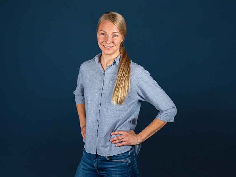 Nainen seisoo kädet lanteilla ja hymyilee.