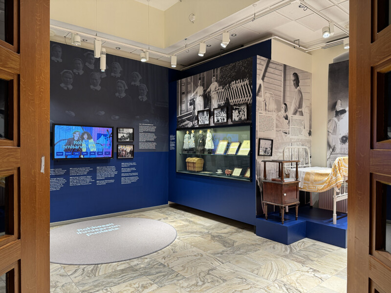 Sisäänkäynti näyttelytilaan, jossa seinillä on valokuvia, tekstejä ja esineitä diakonissalaitoksen historiasta.