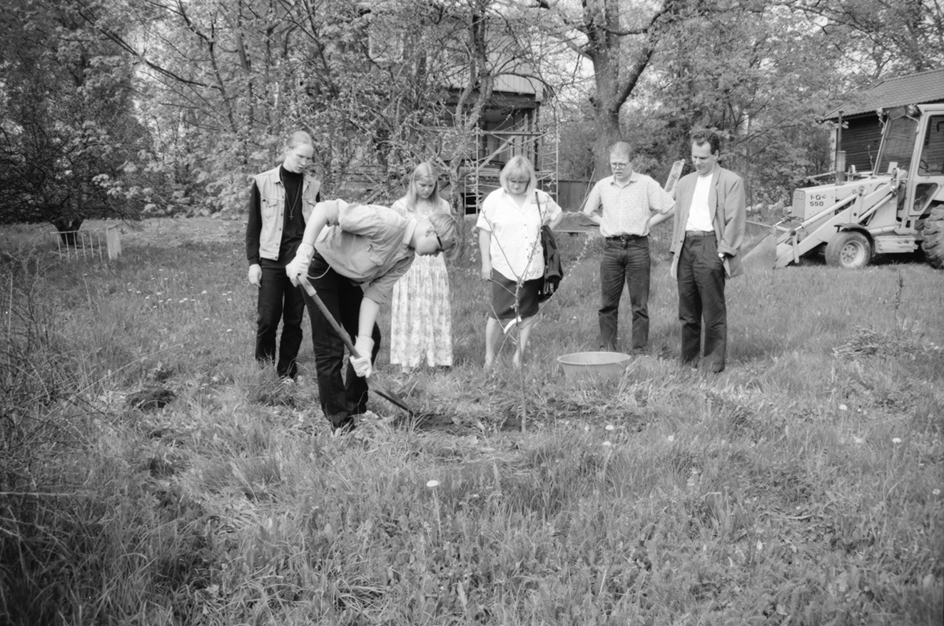 Ryhmä ihmisiä istuttaa omenapuuta.