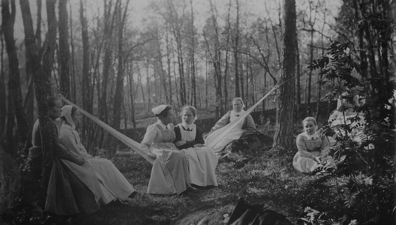 Mustavalkoinen valokuva, jossa useita naisia istuu ja keinuu riippukeinussa metsäisessä ympäristössä.