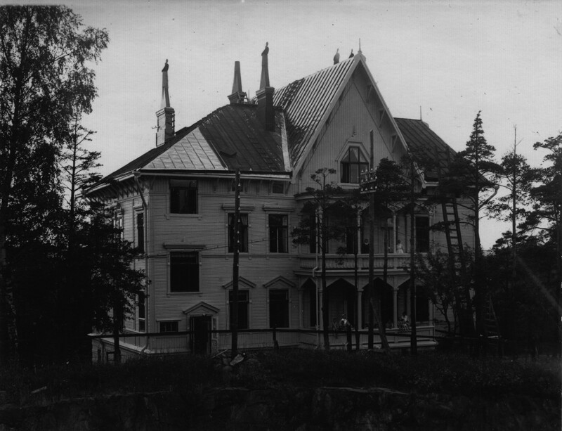 Vanha kolmikerroksinen puurakennus, jonka edessä on muutamia puita ja ympärillä metsämaisema, mustavalkoinen valokuva 1930-luvulta.