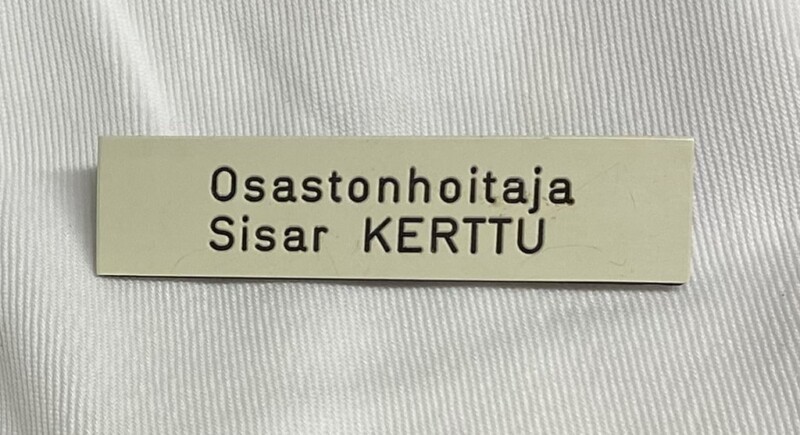 Nimikyltti, jossa lukee "Osastonhoitaja Sisar Kerttu" valkoisella taustalla.
