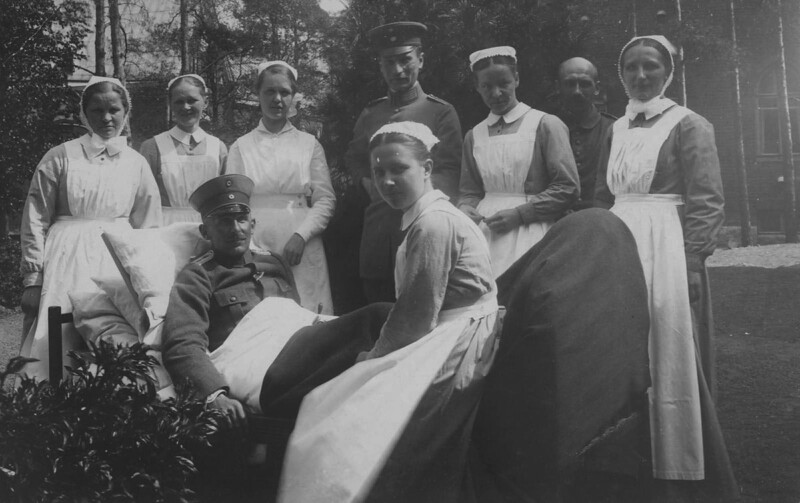Mustavalkoinen kuva, jossa saksalainen sotilas istuu vuoteessa ulkona ja ympärillään useita diakonissoja ja hoitajia vuonna 1918.