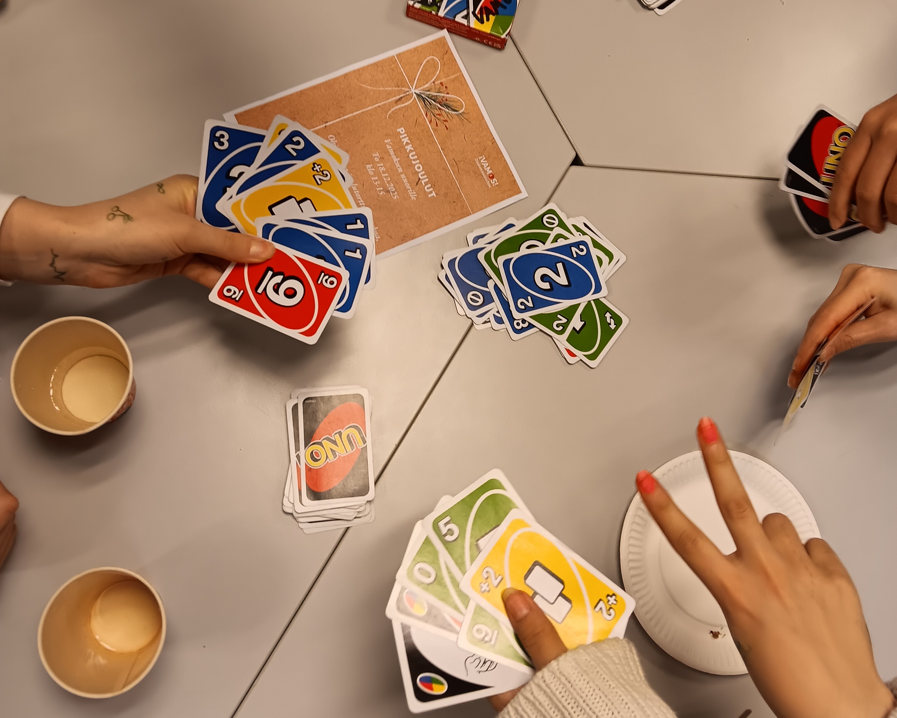 Nuoret pelaavat Uno-korttipeliä pöydän ääressä.