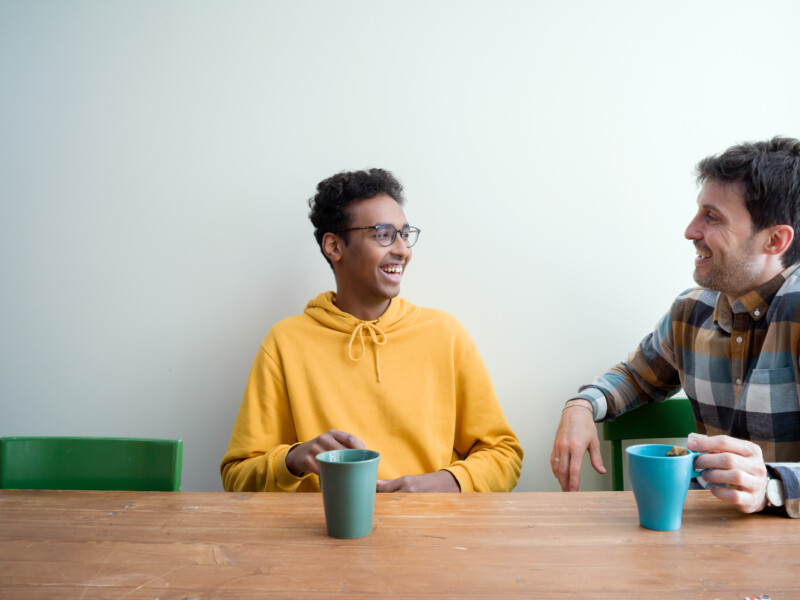 Kaksi miestä istuu pöydän ääressä kahvikupit edessään.