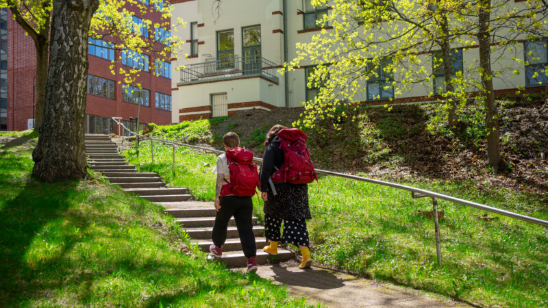 Kaksi reppuselkäistä ihmistä kävelee puistossa.