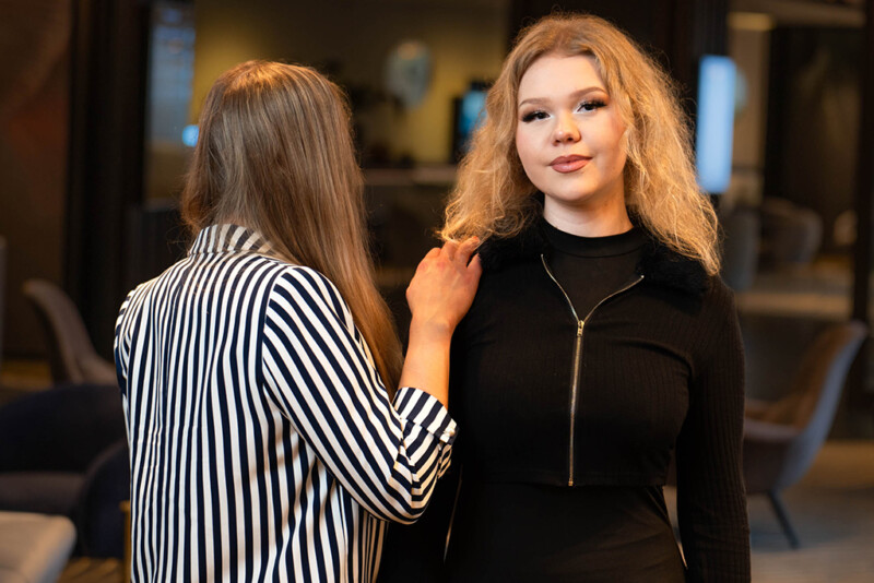 Kaksi henkilöä seisoo vierekkäin, toinen on selin ja toinen katsoo kameraa kohti.