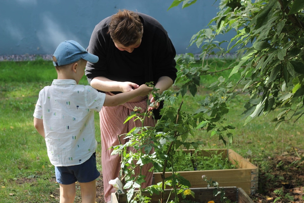Aikuinen ja lapsi tutkivat yhdessä kasvia puutarhassa, taustalla nurmikko ja sininen seinä.