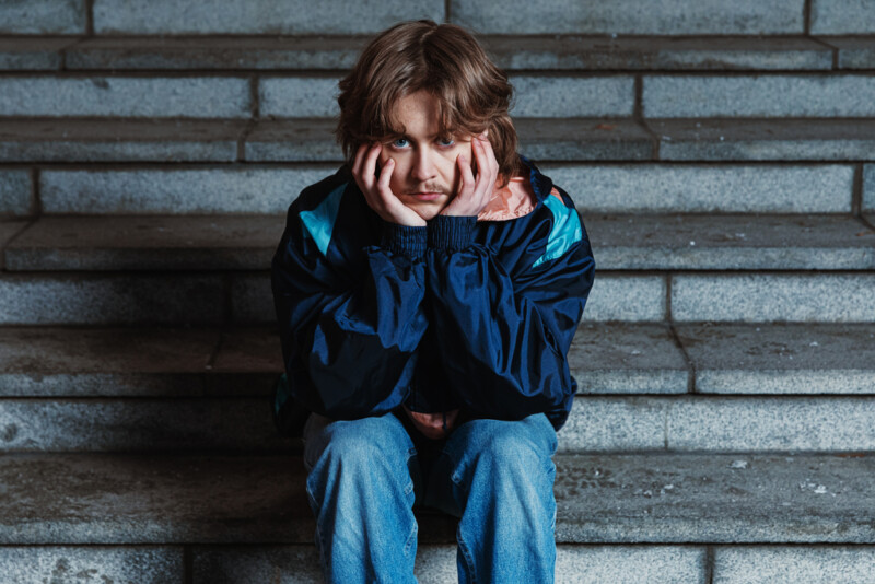 Nuori istuu rappusilla ja nojaa käsiinsä.