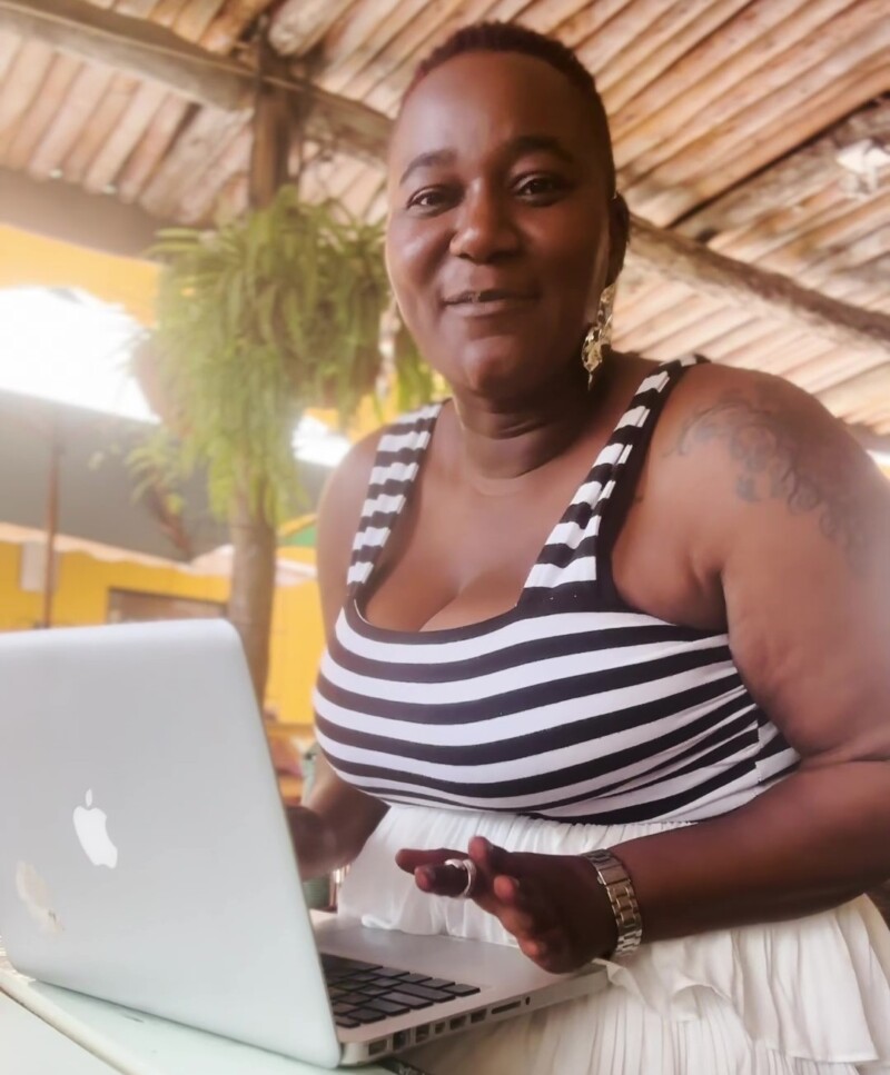 Nainen istuu kahvilassa kannettavan tietokoneen ääressä ja katsoo kameraan.