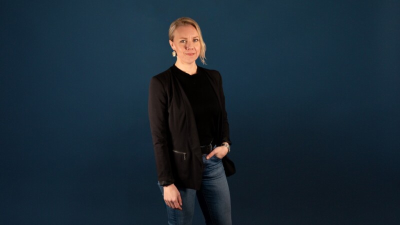 Vaaleahiuksinen nainen seisoo toinen käsi housun taskussa katsoen kameraan.